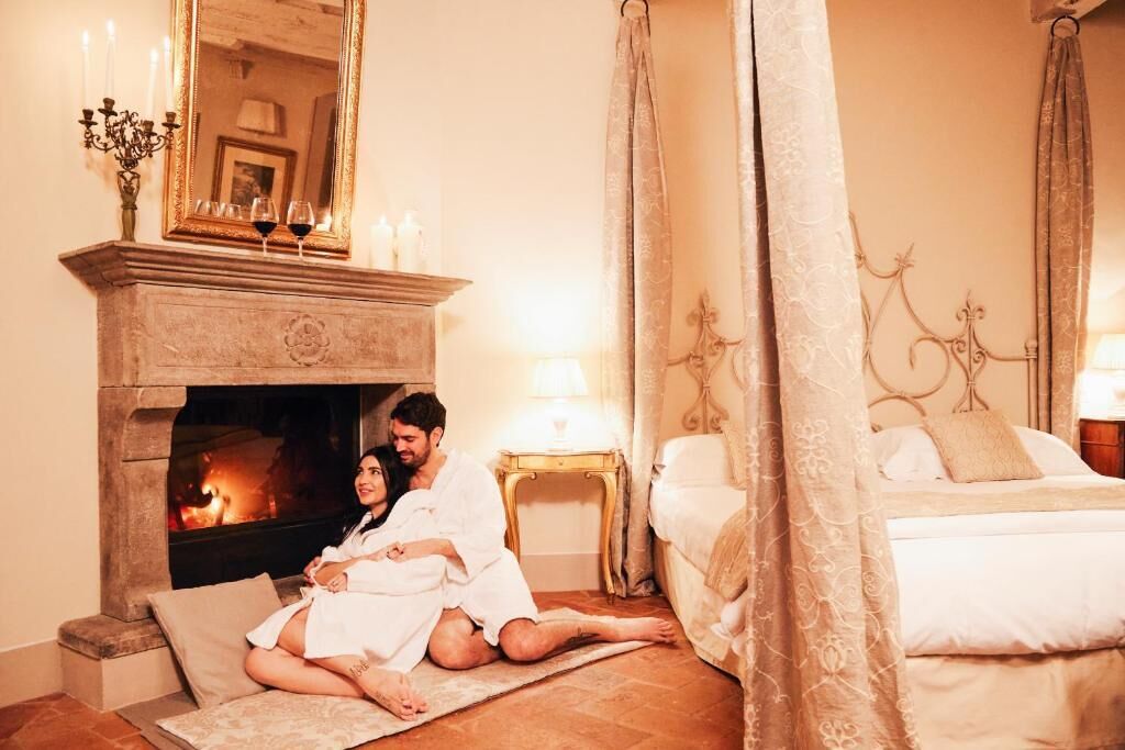 Ein gemütliches Schlafzimmer mit Kamin, einem Himmelsbett und einem Nachttisch mit Lampe.