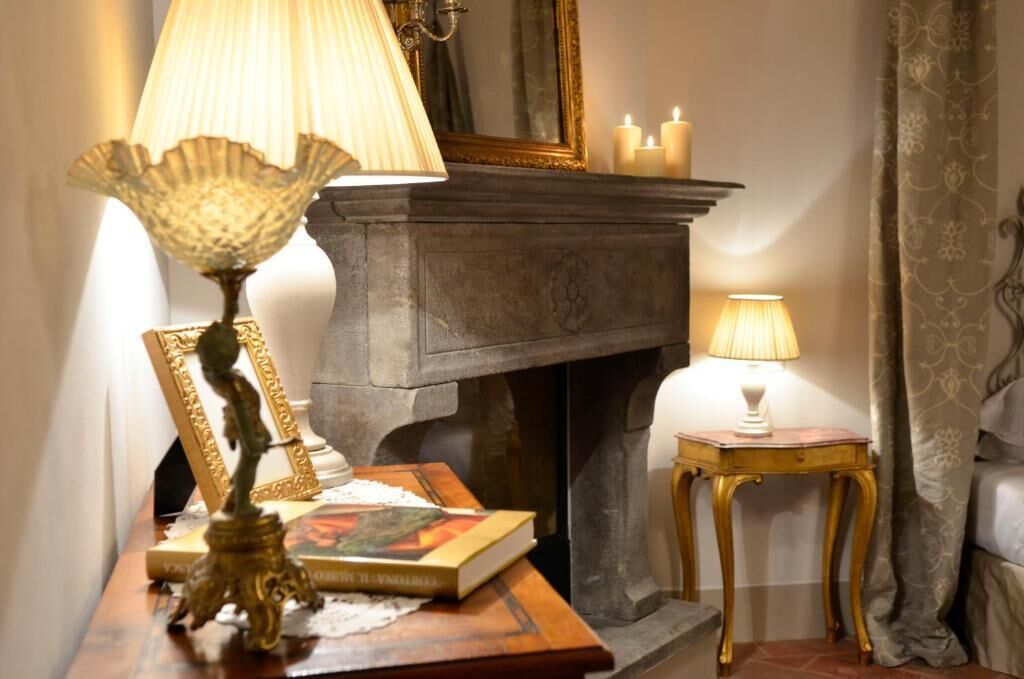 A room with a fireplace, two lamps, a mirror, and a small table with books and a decorative item.