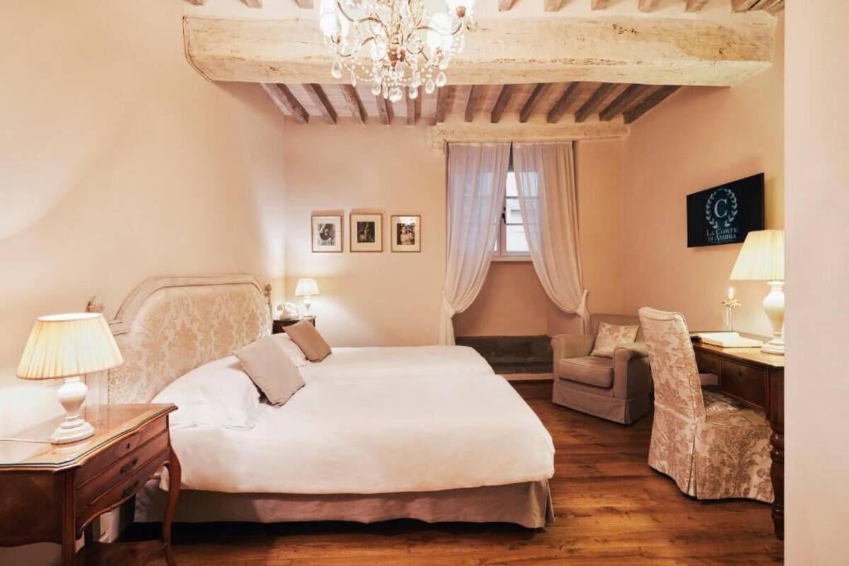 A bedroom with a large bed, a chair, a desk, and a chandelier.