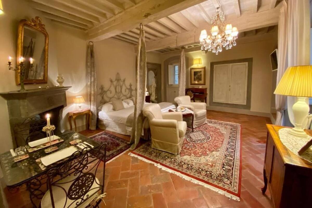 A room with a fireplace, a chandelier, a bed, and a dining area with a table set for two.