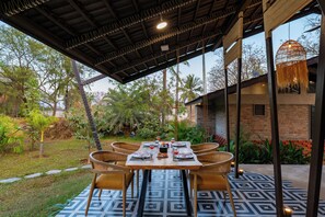 An outdoor dining area with a table set for four, surrounded by wicker chairs, under a covered roof with a patterned floor.