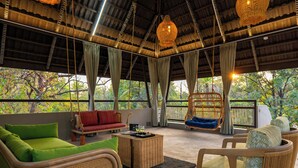 Un amplio espacio exterior con mobiliario de mimbre, una silla colgante y vistas a árboles.