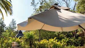 Un área de piscina con sillones reclinables, una sombrilla grande y una estructura de piedra.