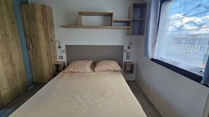 Un dormitorio pequeño y ordenado con una cama individual, dos mesitas de noche, un armario de madera y una ventana con vistas.