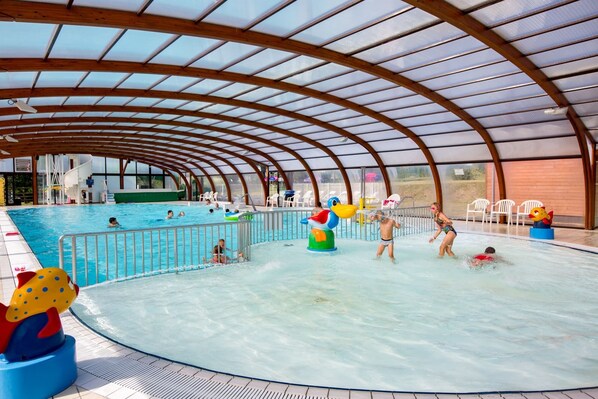 Una piscina interior con techo cubierto, agua cristalina y colorido equipamiento de juegos.