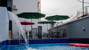 Une piscine dont l’eau dévale en cascade sur un bord carrelé, entourée de chaises longues et de parasols.