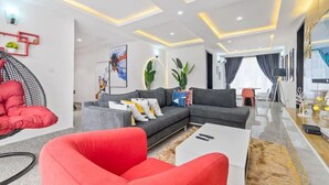 Un salon moderne avec un canapé d’angle gris, un fauteuil rouge et une table basse blanche.