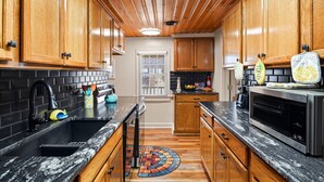A kitchen with wooden cabinets, a black countertop, a stainless steel oven, and a patterned rug. - The Lemon Twist at Carolina Beach (Carolina Beach)