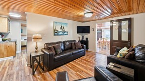 A living room with a wooden ceiling, a leather sofa, a TV, and a painting. - The Lemon Twist at Carolina Beach (Carolina Beach)