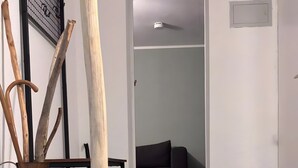 Una escalera conduce a una sala de estar con piso de madera oscura, un jarrón marrón con ramas y una silla negra.
