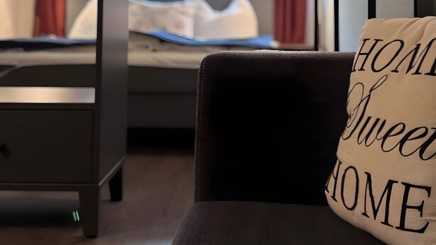 Habitación de hotel con cama, lámparas de noche, ventana con cortinas y almohada con el texto 'HOME Sweet HOME'.