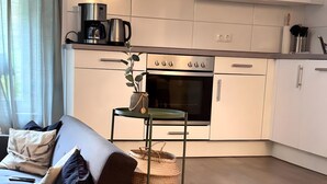 Una cocina moderna con armarios blancos, horno empotrado y cafetera.