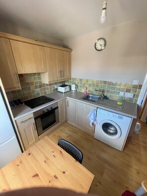 Eine kompakte Küche mit Holzausstattung, einem Backofen, einer Waschmaschine und einem Spülbecken.
