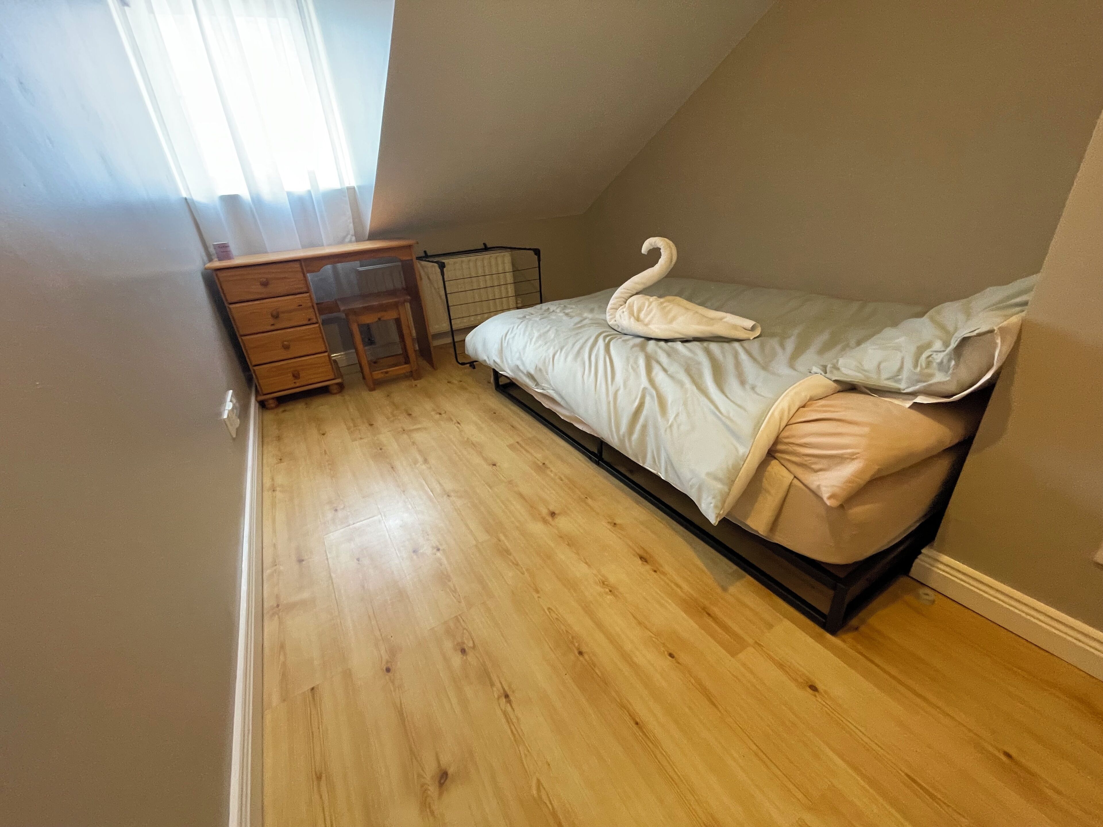 A bedroom with a bed, wooden dresser, and a desk.