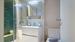 A modern bathroom with a glass-enclosed shower, a white sink with a mirror above, and a toilet with a towel on it. - Athena Urban Retreat Apartment (Athens)