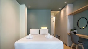 A modern hotel room with a neatly made bed, a desk with a chair, and a round mirror on the wall. - Athena Urban Retreat Apartment (Athens)