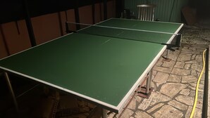 Een tafeltennistafel met net in een kamer met stenen vloer en houten wanden.