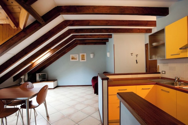 An attic kitchen with exposed wooden beams, a dining area with a table and chairs, and yellow cabinets.