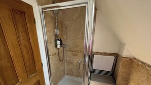 Een doucheomgeving met glazen wanden, een handdouche, een handdoekrek en een klein plankje met toiletartikelen.
