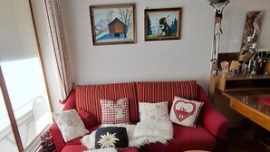 A living room with a red sofa, a round wooden coffee table, and two paintings on the wall. - Apartment 'Älple' with Private Terrace and Wi-Fi (Bad Hindelang)