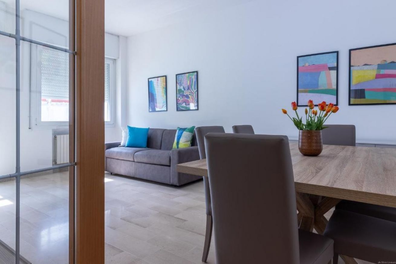 A modern interior with a grey sofa, a wooden dining table, and artwork on the walls.