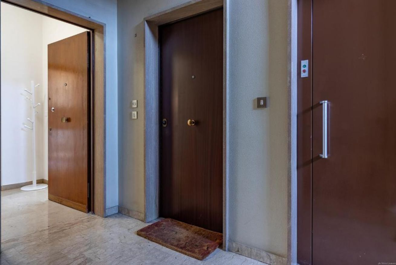 A hallway with three wooden doors, a white floor lamp, and a red doormat.