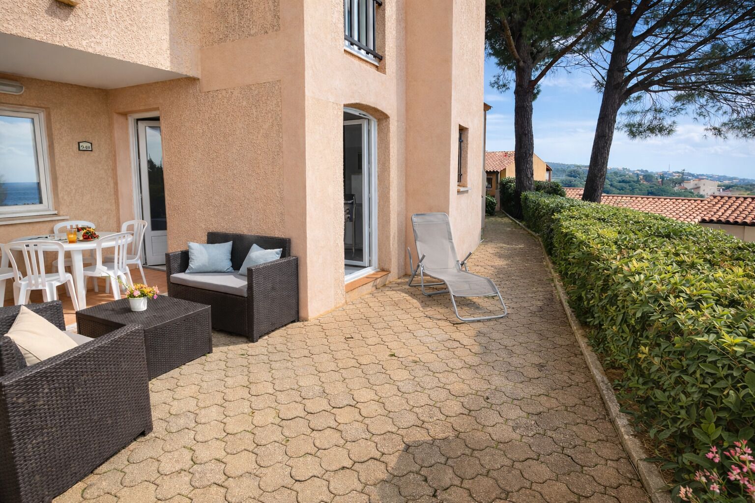 Une terrasse avec des meubles en osier, une table blanche et un fauteuil de relaxation.
