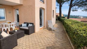 Une terrasse avec des meubles en osier, une table blanche et un fauteuil de relaxation.