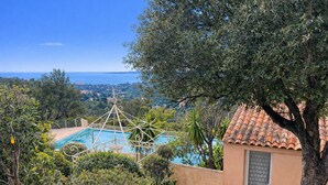 Une piscine dotée d’une structure métallique aux lignes géométriques, entourée d’une végétation luxuriante et offrant une vue sur la mer.