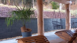 Een houten pergola met daaronder twee loungestoelen, een plant in pot en een zwarte muur op de achtergrond.
