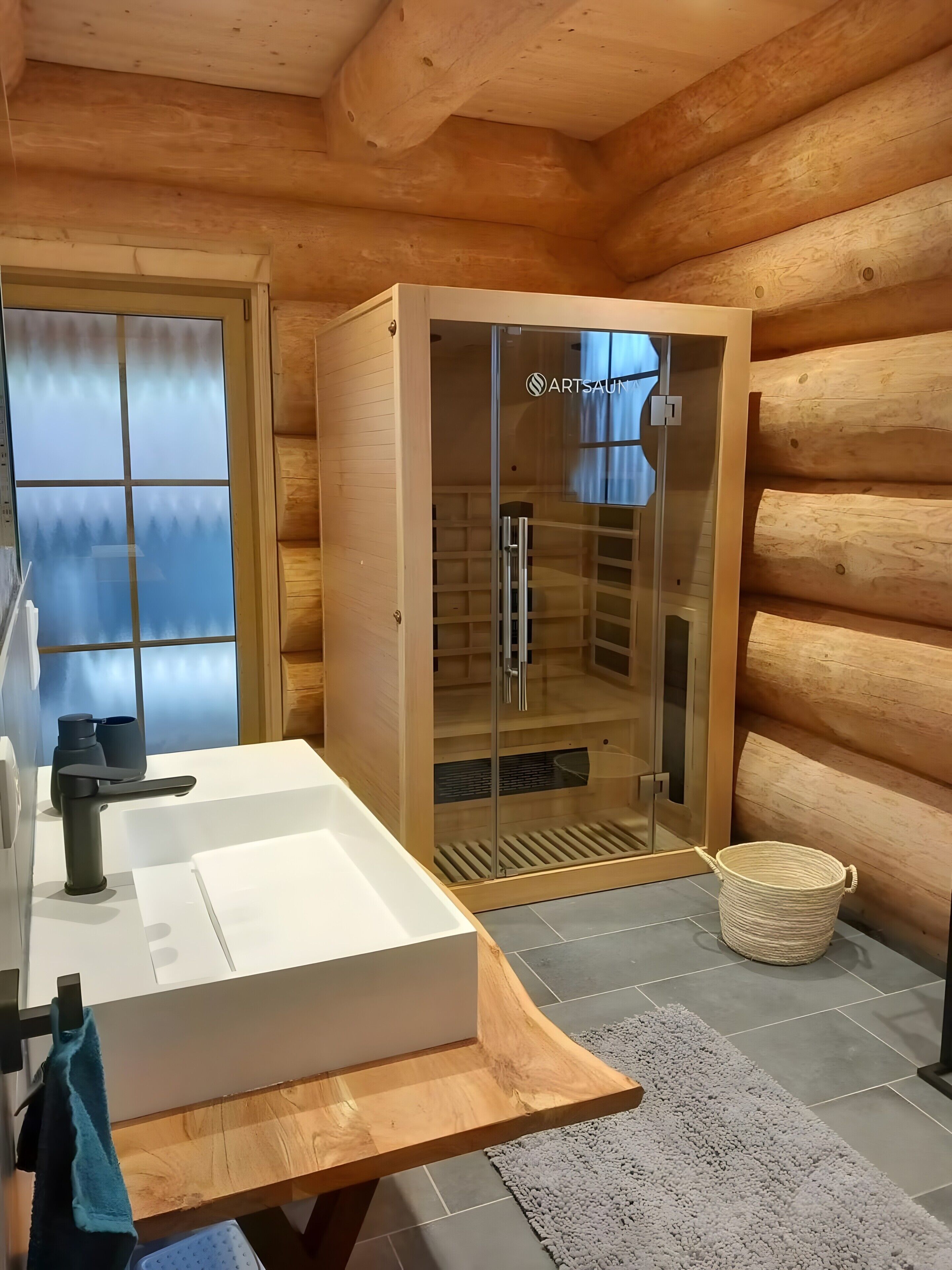L’intérieur d’un chalet en bois comprend un sauna vitré, un évier blanc et un banc en bois.