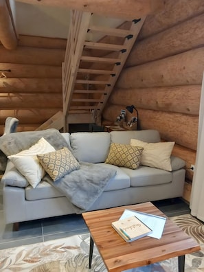 A log cabin interior with a sofa, pillows, a wooden table, and a staircase.
