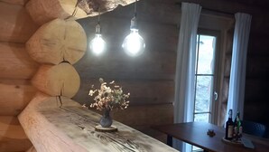 Een rustiek houten interieur met een lange tafel in het midden, hangende lampen en een raam met gordijnen.