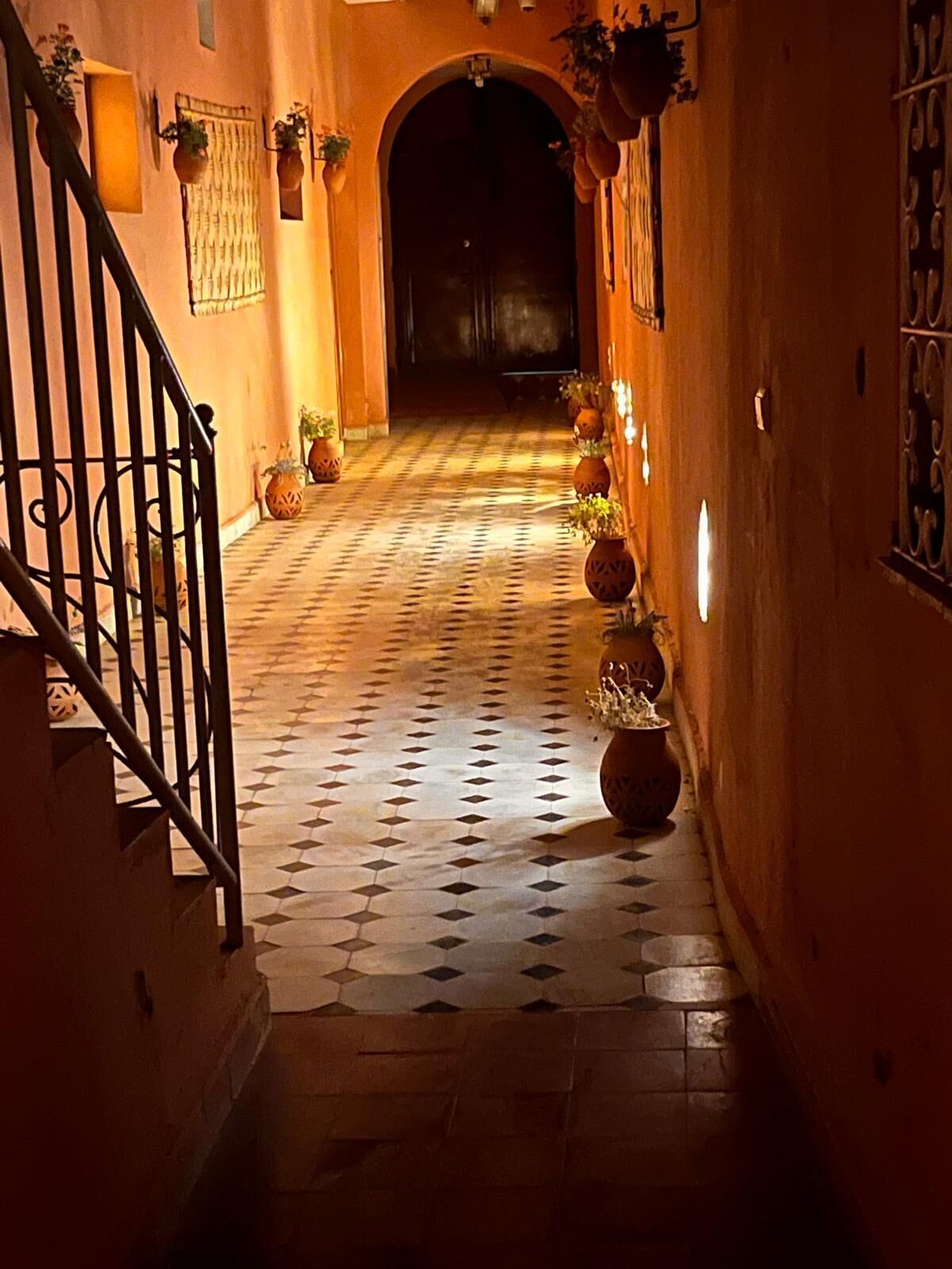 Un pasillo con piso de baldosas, una escalera a la izquierda y plantas en macetas a lo largo de las paredes.