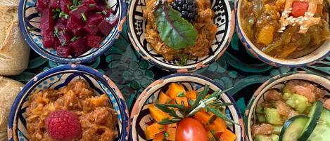A tray with various dishes including beetroot salad, a berry compote, a vegetable stew, a carrot salad, a hummus with a raspberry, and a cucumber salad.
