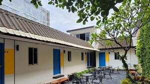 Un patio con asientos exteriores, un edificio con puertas azules y un árbol.