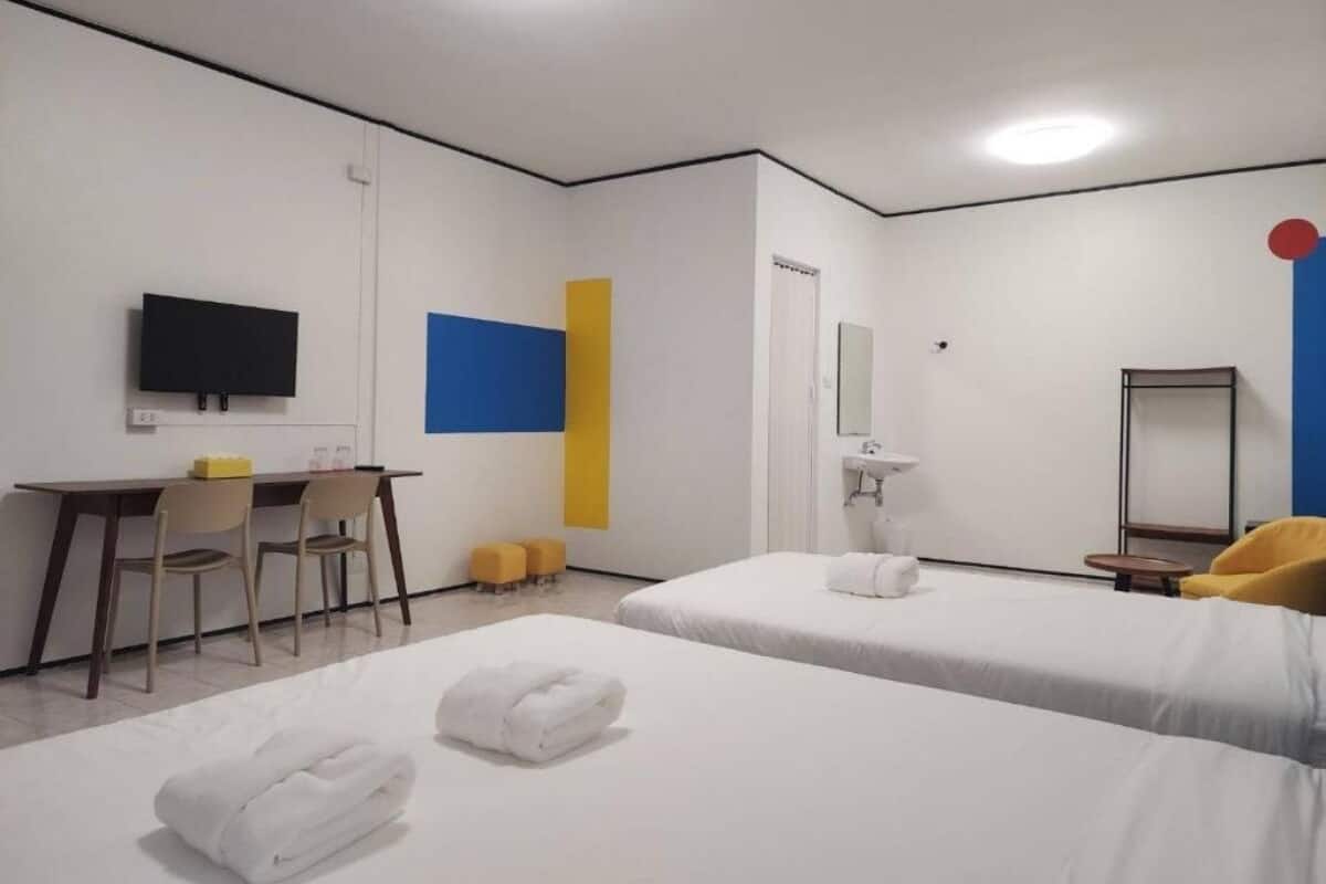 Habitación de hotel con dos camas, un escritorio, una silla, un televisor, un espejo y una mesita.