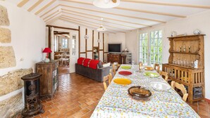 A dining area with a long table, chairs, a television, and a wooden cabinet with glassware.