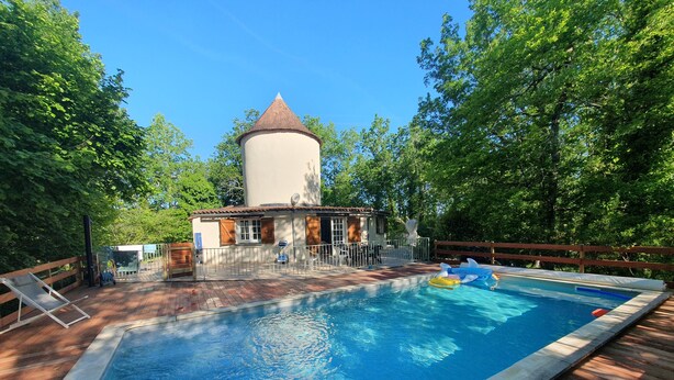 A swimming pool with a wooden deck, a small building with a conical roof, and a fenced area.