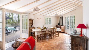 An open-plan living and dining area with a wooden ceiling, a dining table set for four, and a red sofa.