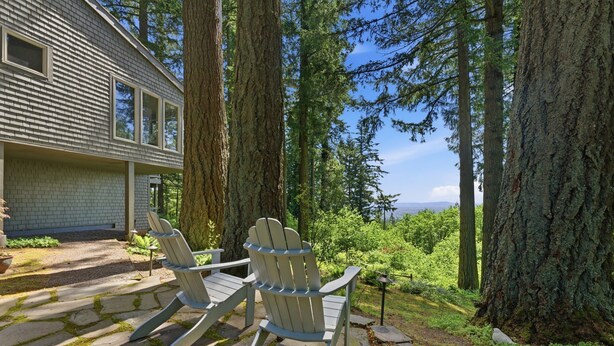Een huis met terras, twee Adirondack-stoelen en uitzicht op bos en bergen.