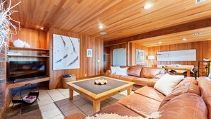 Een houten interieur met een bank, een salontafel, een televisie en kunstwerken aan de wanden.