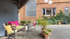Eine Terrasse mit Tisch und Stühlen, Blumentöpfen und einem Ziegelgebäude mit einem Fenster.