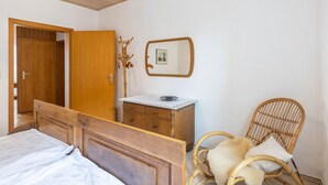 A bedroom with a wooden bed, a wooden dresser, a wicker chair, and a mirror on the wall. - Apartment 'Hofhausnr3' with Private Terrace, Garden, and Wi-Fi (Warburg)