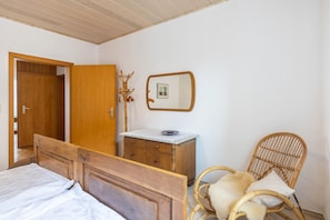 A bedroom with a wooden bed, a wooden dresser, a wicker chair, and a mirror on the wall. - Apartment 'Hofhausnr3' with Private Terrace, Garden, and Wi-Fi (Warburg)