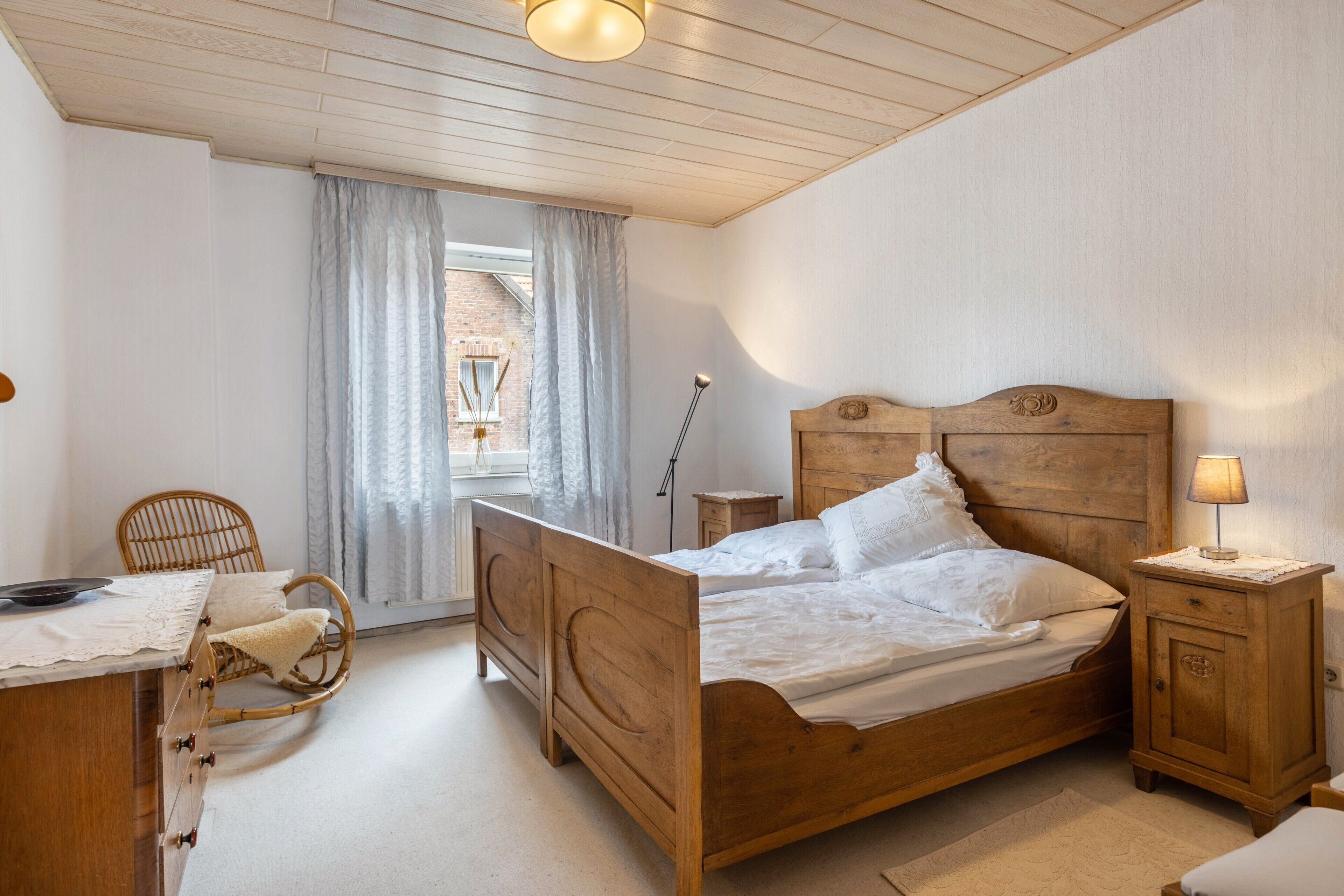 A bedroom with a wooden bed, a bedside table with a lamp, a chair, and a desk with a lamp.