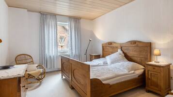 A bedroom with a wooden bed, a bedside table with a lamp, a chair, and a desk with a lamp.