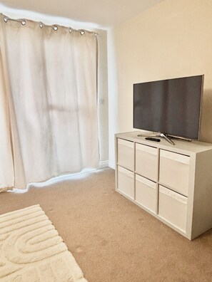 A room with a large window, a flat-screen TV on a cabinet, and a beige carpet. - That White Place (Exeter)
