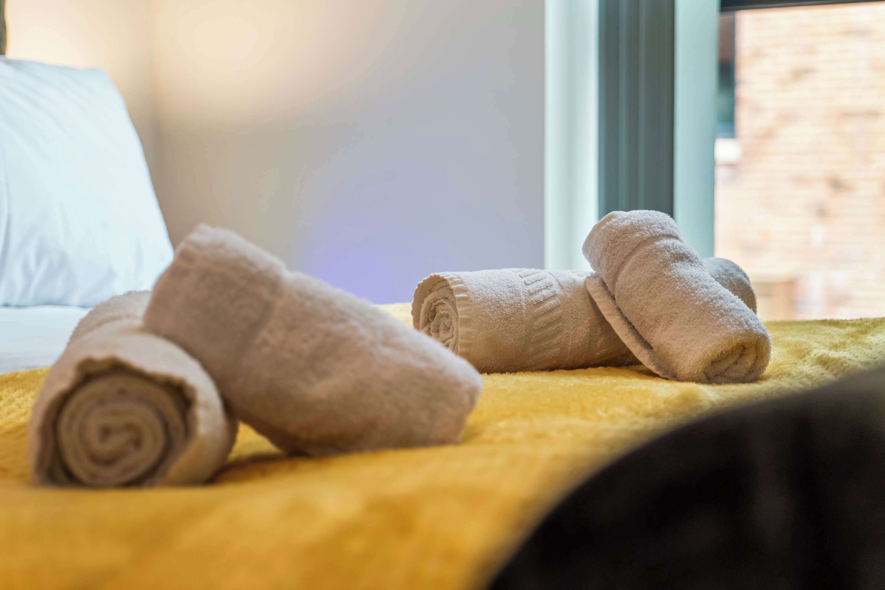 Un letto con asciugamani arrotolati e una coperta gialla.