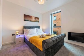 A modern bedroom with a bed, bedside lamp, artwork, and a window with a view of a brick building. - Stylish City Centre Apartment - Heart of Jewellery (West Midlands)